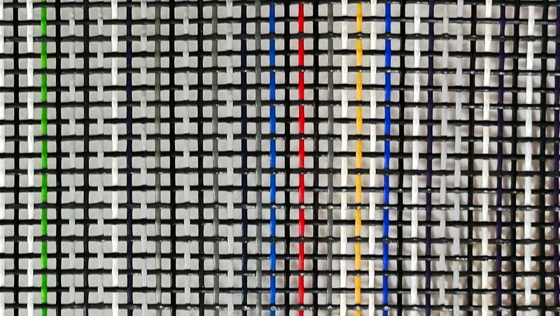 Close-up of Multi-Mesh HD dump truck tarp material showing random colored yarns in green, blue, red, and yellow woven into a 54% closed weave pattern